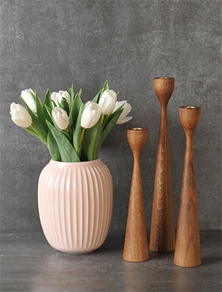 Das Bild zeigt 3 Rolf-Holz-Kerzenständer in unterschiedlichen Höhen aus dunkelbraun gebeiztem Eichenholz zusammen mit einer mittelgroßen Hammershøi-Vase aus roséfarbener Keramik. In der Vase steht ein Strauß weißer Tulpen.