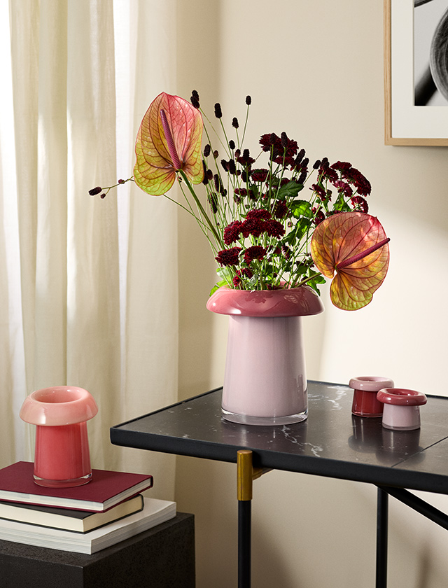 Holmegaard Soma Vasen in Koralle und Rosa aus mundgeblasenem Glas, dekoriert mit einem farbenprächtigen Blumenstrauß auf einem schwarzen Beistelltisch.