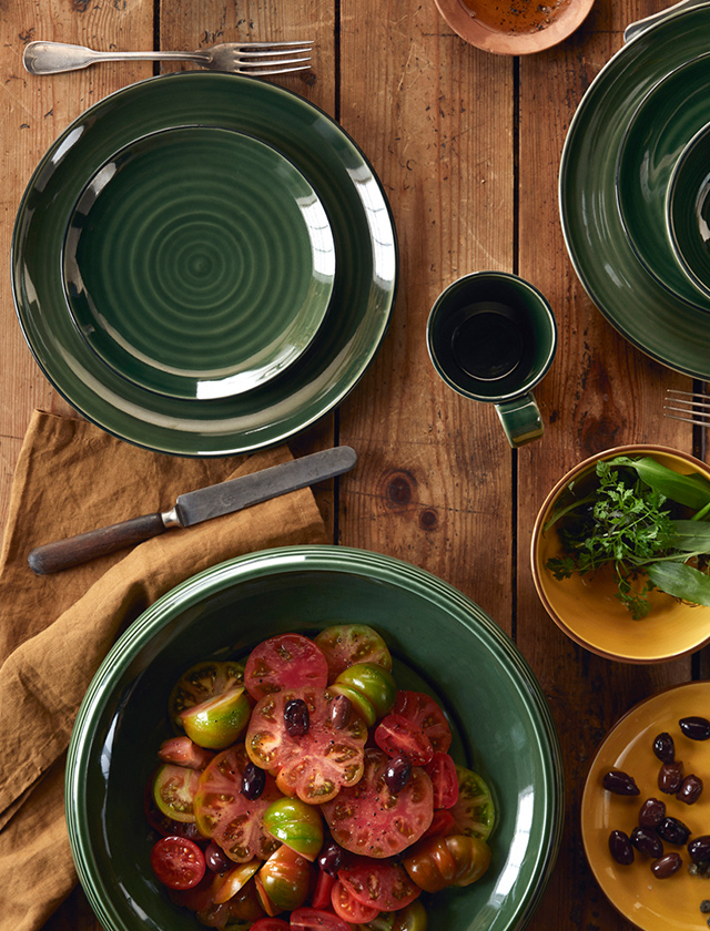 Sommerlich gedeckter Tisch mit der Colore Geschirrserie von Kähler Design in Sage Green und Saffron Yellow - Salatschüssel mit Tomnatensalat sowie Frühstücksteller & Essteller und Müslischalen.