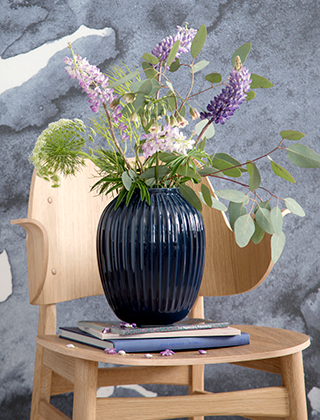 Die Hammershøi Vase in der großen Größe in Indigoblau von Kähler Design, abgestellt auf einen Plywood Chair und einen wundervollen Gartenstrauß mit sommerlichen Blumen.