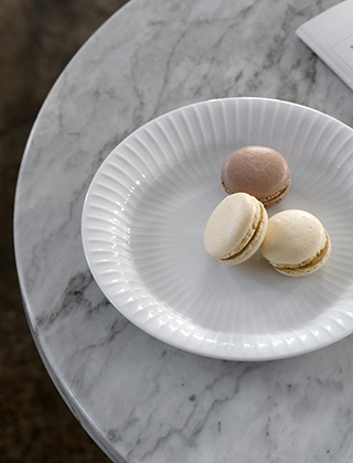 Drei Macarons (französisches Baisergebäck aus Mandelmehl) auf einem kleinen Kuchen-Teller aus weißem Porzellan von Kähler Design. Der Teller steht auf einem Marmortisch.