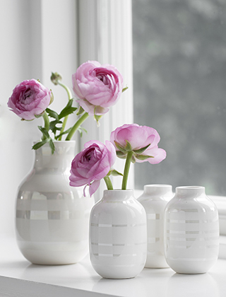 Perlmuttfarbene Omaggio Miniatur Blumenvasen im 3er-Set auf dem Fensterbrett stehend. Im Hintergrund steht eine kleine perlmuttfarbene Omaggio-Vase gefüllt mit rosafarbenen Ranunkeln.