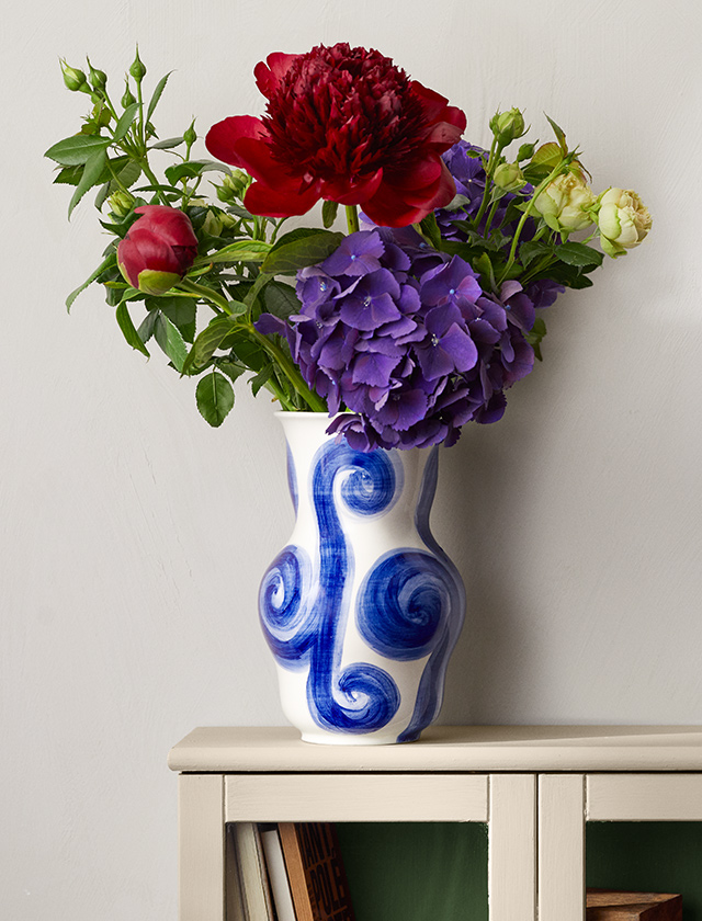 Die große 22 cm hohe Tulle Vase von Kähler Design eignet sich für größere Blumensträuße und verleiht durch ihr einzigartiges Design und ihre kunstvollen Verzierungen jedem Raum eine elegante und künstlerische Note. Ihre cremeweiße Grundfarbe und blauen Wirbeln können sowohl in klassischen als auch in modernen Einrichtungsstilen harmonieren und bieten einen reizvollen Blickfang, der die Schönheit der Blumen unterstreicht und die Ästhetik des Wohnraums bereichert.