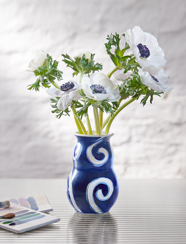Die mittlere Tulle Vase ist 12,5 cm groß, hat eine dunkelblaue Grundfarbe mit weißen Wirbeln und einer Glasur, die ihr Tiefe und Lebendigkeit verleiht. Die klaren, organischen Pinselstriche sind von Tulle Emborg, einer der talentiertesten Malerinnen ihrer Zeit, und geben der Vase ein einzigartiges und authentisches Aussehen. Die Vase wurde nach ihr benannt und zeichnet sich durch ihren künstlerischen Ausdruck in einem modernen Kontext aus. Ihre abgerundeten Formen und die tiefe, satte Glasuren machen sie zu einem kleinen Kunstwerk, das auch ohne Blumen als dekoratives Element in einer zeitgenössischen Einrichtung dient.