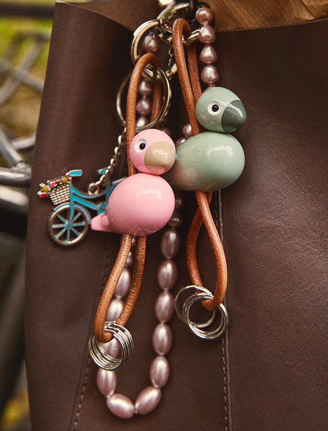 Kay Bojesen Singvögel Schlüsselanhänger in Rosa und Mintgrün, dekorativ am Taschenriemen befestigt.