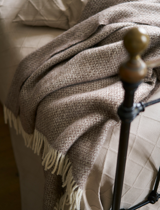 Premium-Decke Lima, 40 % Alpakawolle und 60 % Lammwolle. Die Decke hat ein klassisches Muster und ist sowohl ein wärmendes als auch dekoratives Detail, das perfekt ist, um sich an kühlen Abenden darin einzuhüllen.